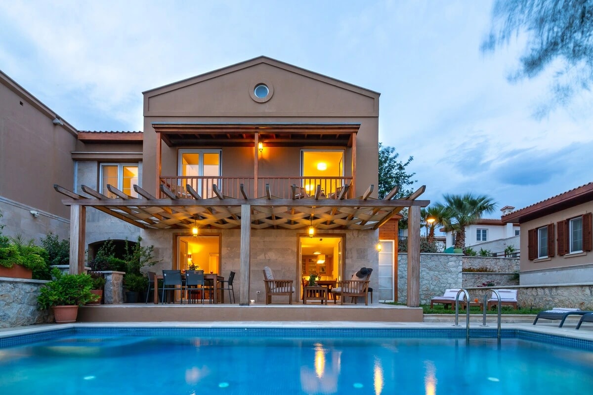 Two-story villa with illuminated terrace and private pool at dusk.