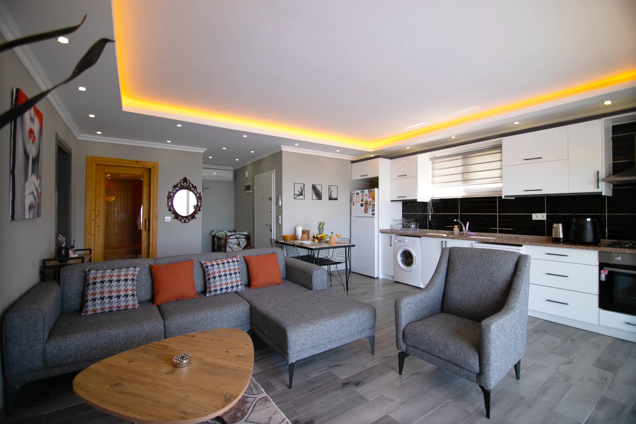 Open-plan living room with gray seating, ambient lighting, and connected kitchen space.