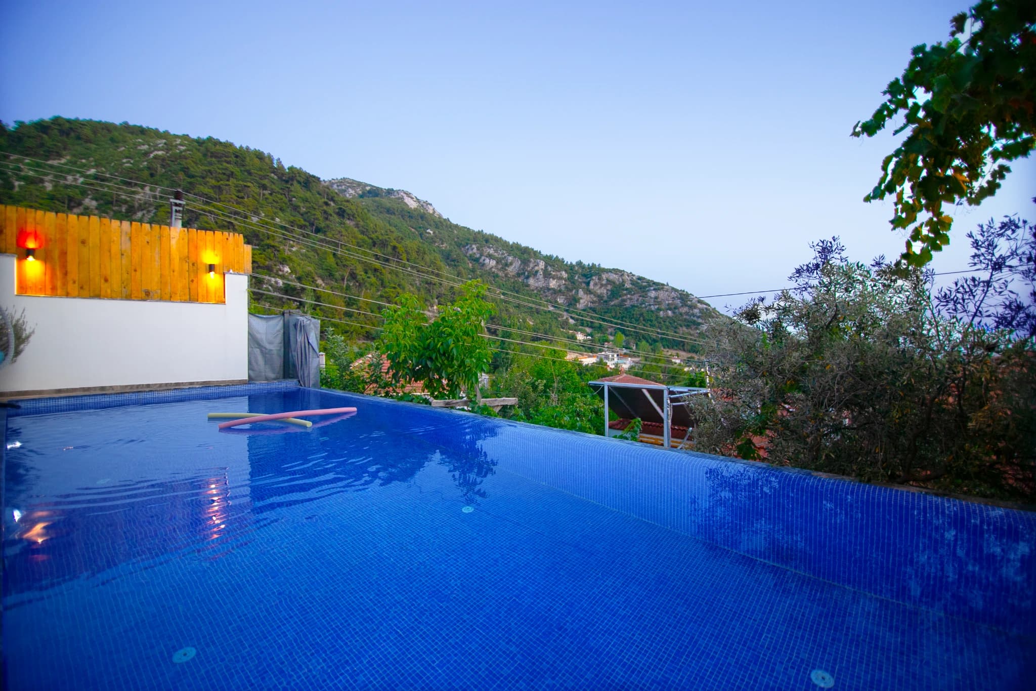 Illuminated pool overlooking lush hillside terrain at twilight.