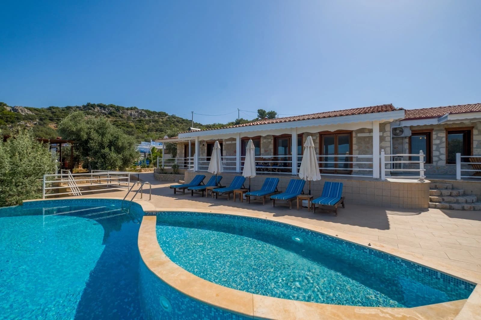 Pool area with multiple loungers and shaded terrace adjacent to main building.