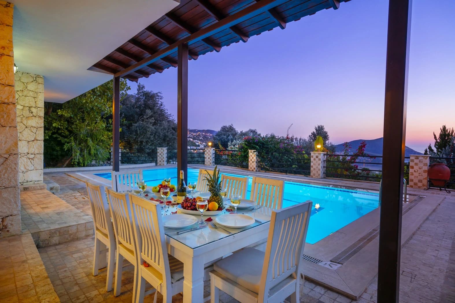 Covered outdoor dining area overlooking the illuminated pool at sunset.
