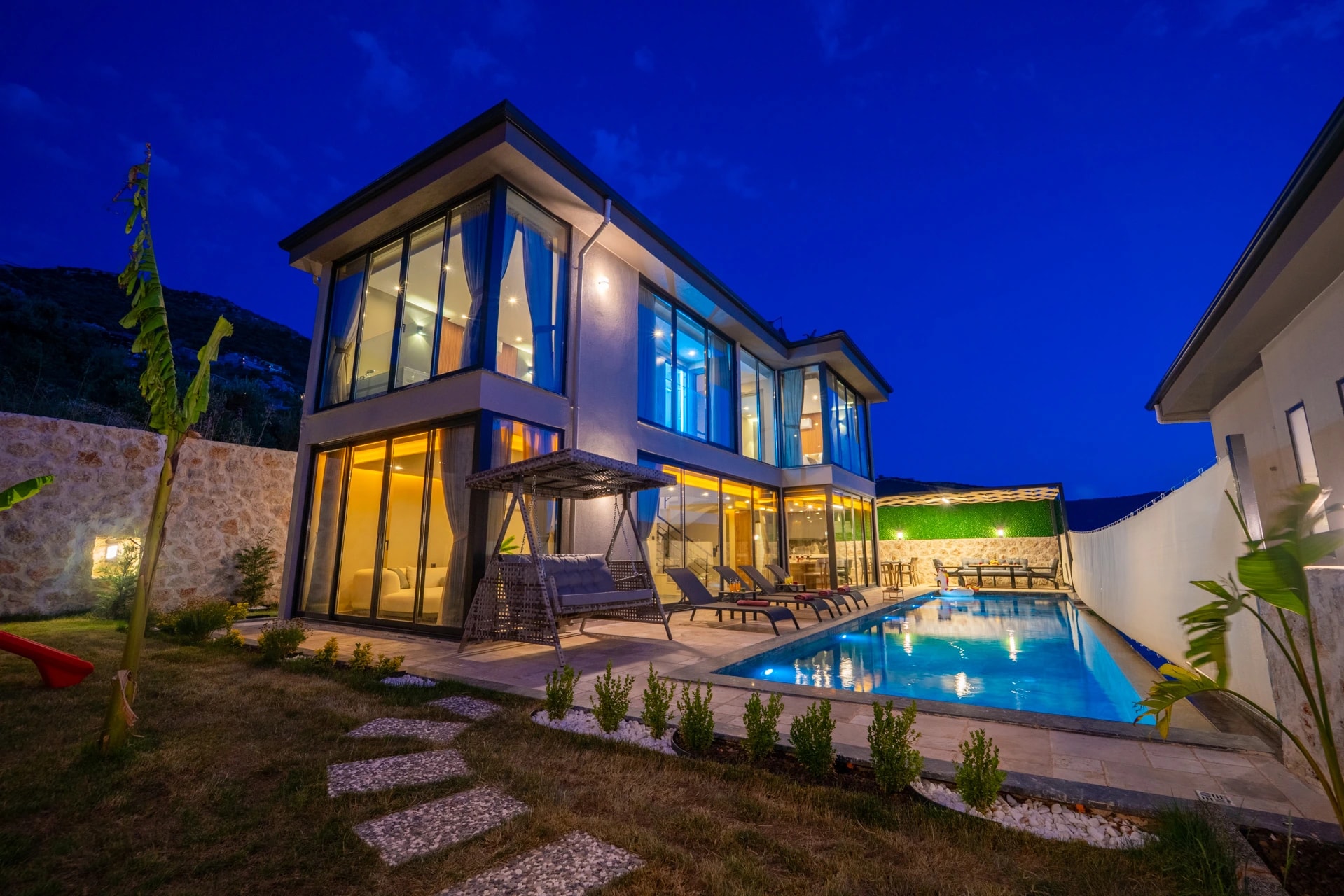 Stunning night view of villa exterior with illuminated private pool and lounge area.
