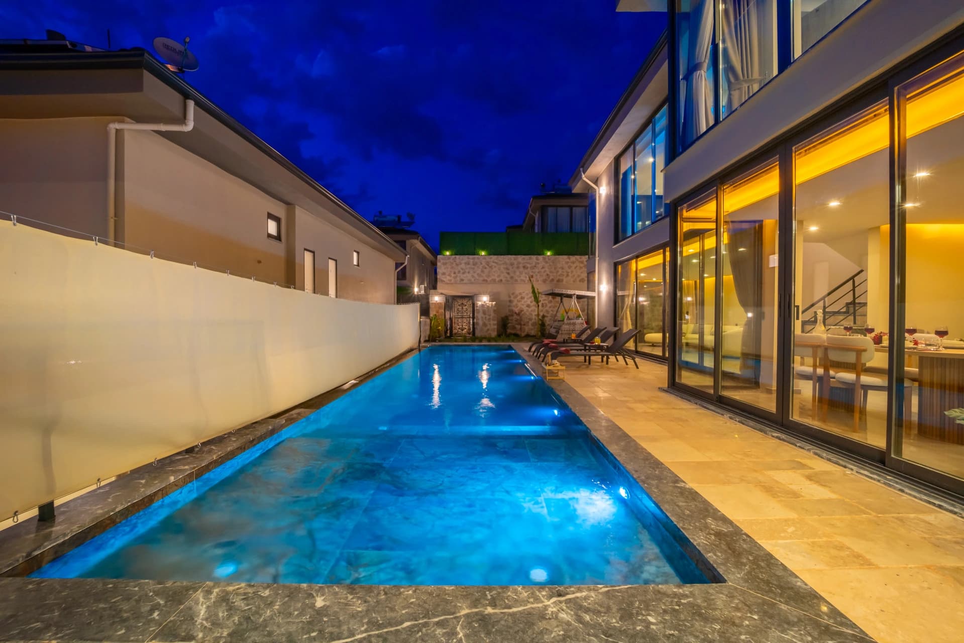 Elongated illuminated private pool viewed from the villa terrace at twilight.