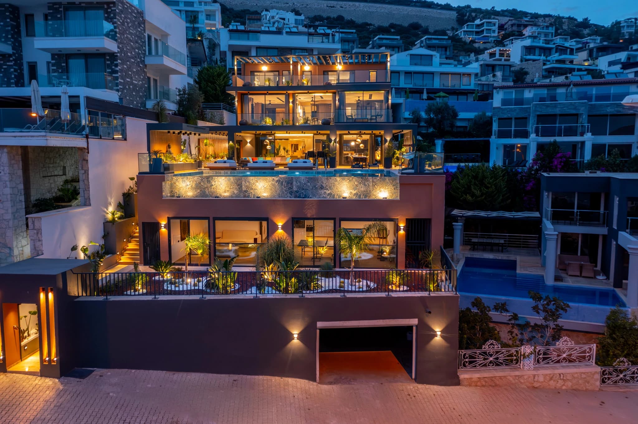 Stunning modern villa exterior at twilight with illuminated facades and urban hillside setting.
