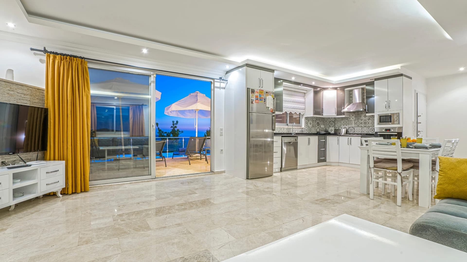 Abgeschiedene 2-Zimmer-Villa mit beheiztem Pool und Berg- & Meerblick in Kalkan – Modern open-plan living and dining area with kitchen, overlooking pool and sea.