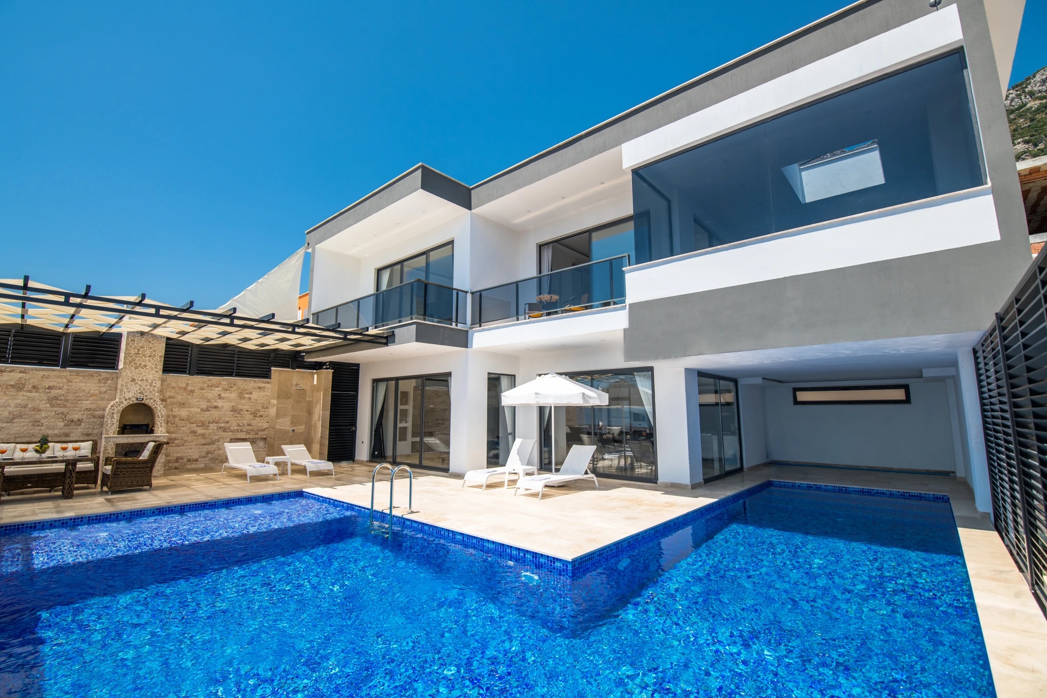 Abgeschiedene Flitterwochen-Villa mit privatem und beheizbarem Innenpool in Kalkan – Modern villa exterior with large swimming pool, sun loungers, and outdoor seating area in bright daylight.