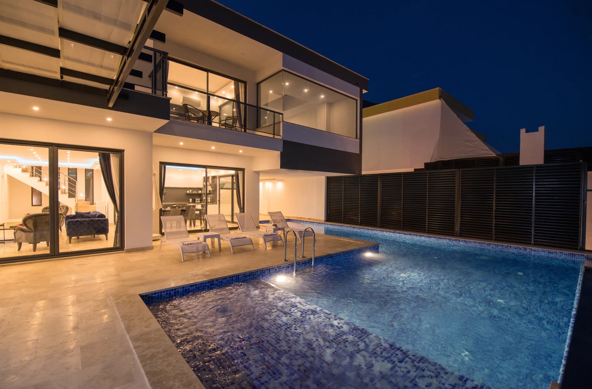 Abgeschiedene Flitterwochen-Villa mit privatem und beheizbarem Innenpool in Kalkan – Stunning nighttime pool area with illuminated water, sun loungers, and modern villa interior visible through glass doors.