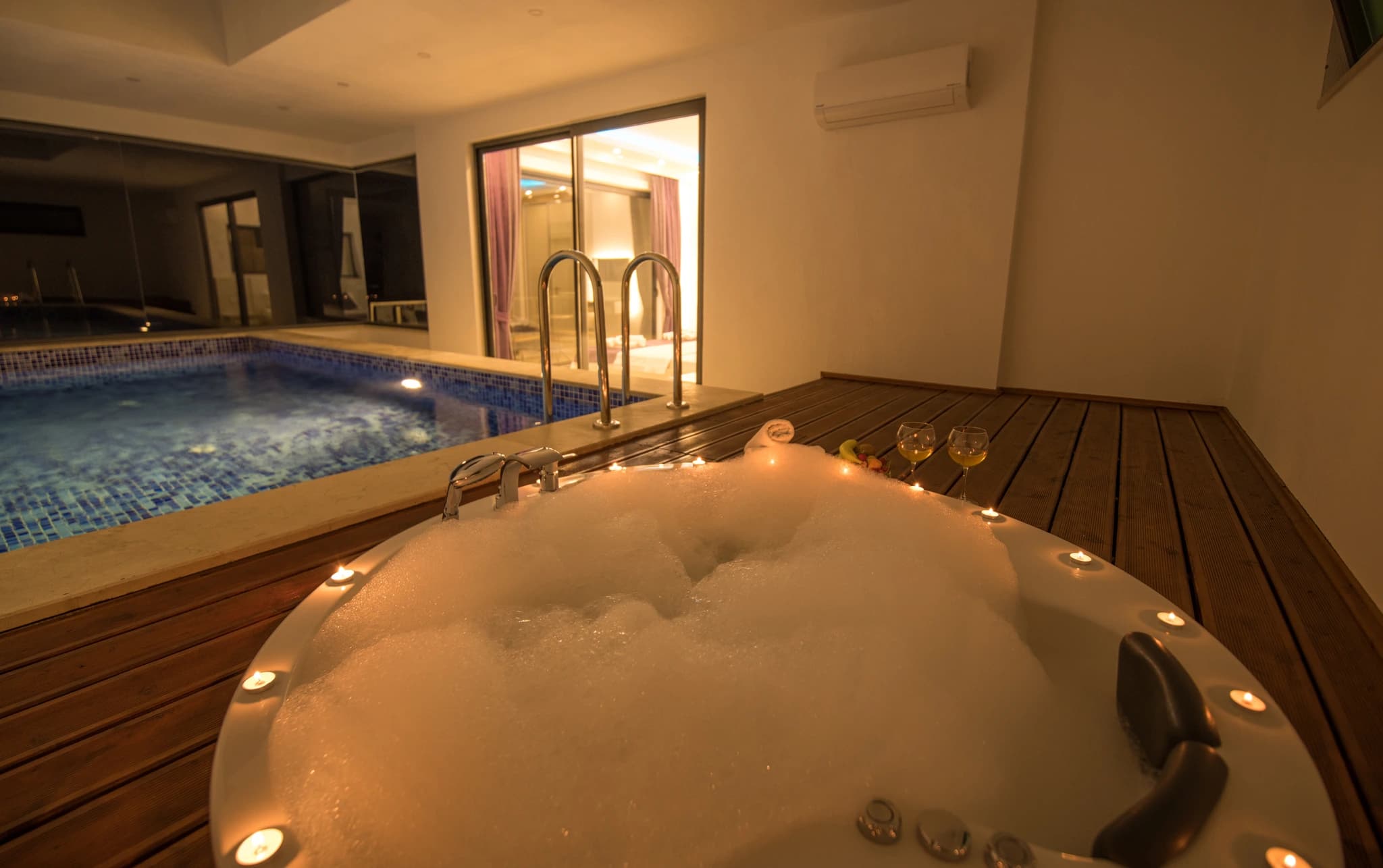 Abgeschiedene Flitterwochen-Villa mit privatem und beheizbarem Innenpool in Kalkan – Luxurious indoor spa with hot tub in foreground and swimming pool, beautifully lit for evening relaxation.