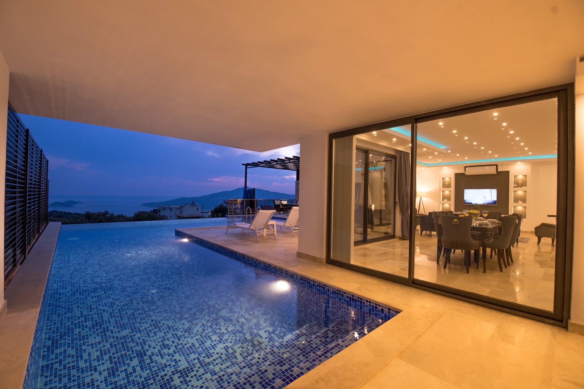 Abgeschiedene Flitterwochen-Villa mit privatem und beheizbarem Innenpool in Kalkan – Stunning illuminated pool overlooking mountains, with adjacent terrace and lounge chairs.