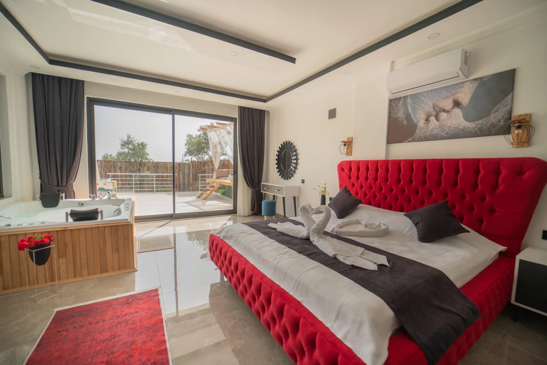 Elegant bedroom with luxurious red bed, spa tub, and private balcony overlooking grounds.